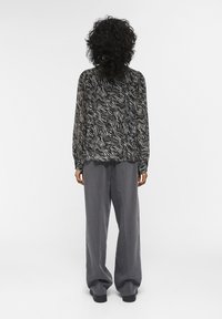 Langarmige zwarte blouse met crèmekleurig zebra-patroon in een relaxte pasvorm, gecombineerd met hooggetailleerde, losse grijze broek.