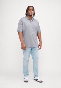 Polo shirt grigio a maniche corte, design con colletto. Abbinato a jeans azzurri chiari e sneaker bianche con strisce nere. Aspetto semplice e classico.
