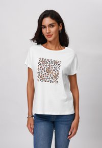 Bijela pamučna majica s okruglim izrezom, koja ima grafiku s uzorkom leoparda u nijansama smeđe, crne i narančaste boje. Kratki rukavi.