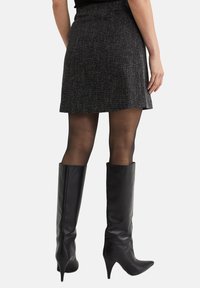 Bottes noires montantes avec des bouts pointus et un talon aiguille, associées à une mini-jupe grise texturée et des collants noirs transparents.