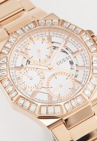 Montre en or rose avec un cadran blanc, trois sous-cadrans et des accents en cristal rectangulaire sur la lunette. Bracelets en métal avec finition polie.