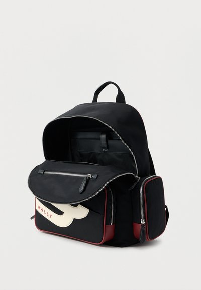 Μαύρο σακίδιο πλάτης με κόκκινα περιγράμματα, εμπρόσθιες και πλαϊνές τσέπες με φερμουάρ, εμπρόσθιο καπάκι τσέπης μερικώς ανοιχτό που δείχνει ένα λογότυπο και εσωτερικό διαμέρισμα.