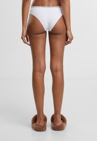 White cotton bikini underwear with a lace trim waistband, viewed from the back. Soft texture with a slightly high-cut design.