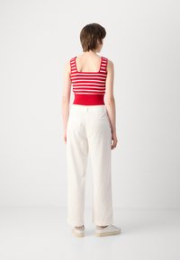 Débardeur rayé rouge et blanc avec un décolleté carré, associé à un pantalon large crème et des baskets blanches, montrant un tissu texturé.