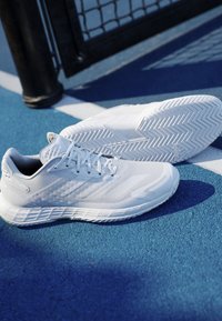 Balti sporta apavi ar teksturētu sietu augšdaļu, plakanu auklu un elegantu dizainu. Apakšzolei ir zivsaskaņas raksts un izliekta forma.