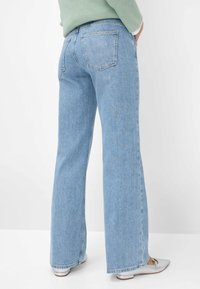 Lichtblauwe, high-waisted jeans met een wide-leg snit. Bevat twee achterzakken en een subtiele vervaging in de textuur. Gedragen met lichtgekleurde schoenen.