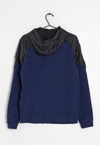 Mörkblå hoodie med svarta nylonaccenter på axlar och huva, med en texturerad tyg, sidofickor och en dragkedja längst ner.