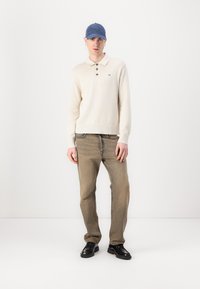 Krämfärgad stickad polotröja med krage och tre knappar, ihop med beige denimjeans och svarta klädsko. Blå keps ger en extra detalj.