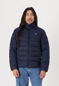 Jachetă bomber marine cu guler înalt, fermoar frontal și model matlasat orizontal. Prezintă un logo mic pe piept.