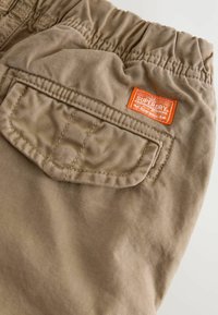 Khaki bomullsbukser med elastisk midjeband, med en baklomme och en orange "Superdry"-logotyp. Mjuk, hållbar tyg.