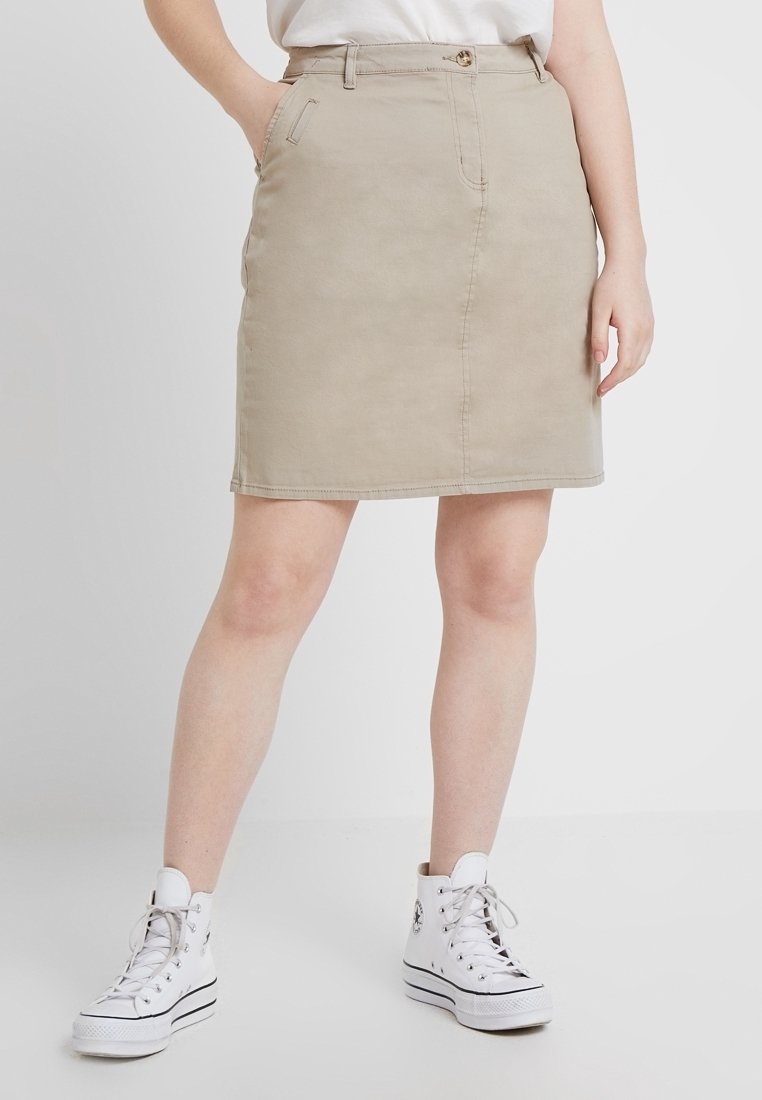 Jupe en denim beige avec poches avant, fermeture à boutons et coutures apparentes. Associée à des baskets montantes blanches.