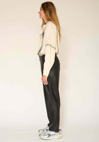 Blouse crème à manches longues avec des détails de couture noirs, portée avec un pantalon en cuir noir et des chaussures de sport argentées. Textures lisses et silhouette ajustée.