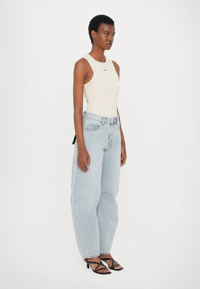 Crème mouwloze top, lichtblauwe baggy jeans en zwarte strappy hakken. De jeans hebben een ontspannen pasvorm en gescheurde details.