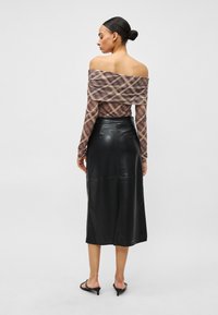 Plecu daļā brīvs rūtainas faktūras brūnas un bēšas krāsas tops, kombinēts ar melnu ādas midi svārku. Gluda virsma un pieguloša vidukļa dizains.