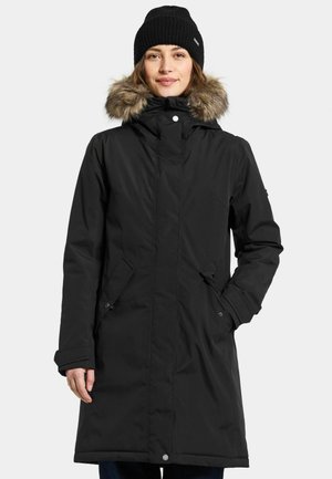 Zwarte waterdichte parka met een met bont gevoerde capuchon, voorzakken en knoopsluitingen. Heeft een rechte snit en een gebreide ribbeanie.
