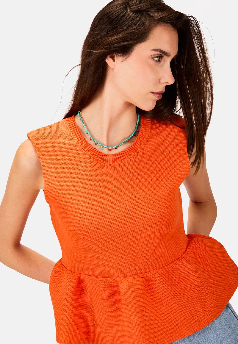 Orange strikket ærmeløs peplum top med ribbet halsudskæring og struktureret talje, suppleret af et lagdelt turkis perlekæde.