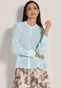 Helles blaues, durchsichtiges Blusenshirt mit rundem Halsausschnitt, Knopfleiste vorne und langen Ärmeln, kombiniert mit einer Hose im Blumendesign.