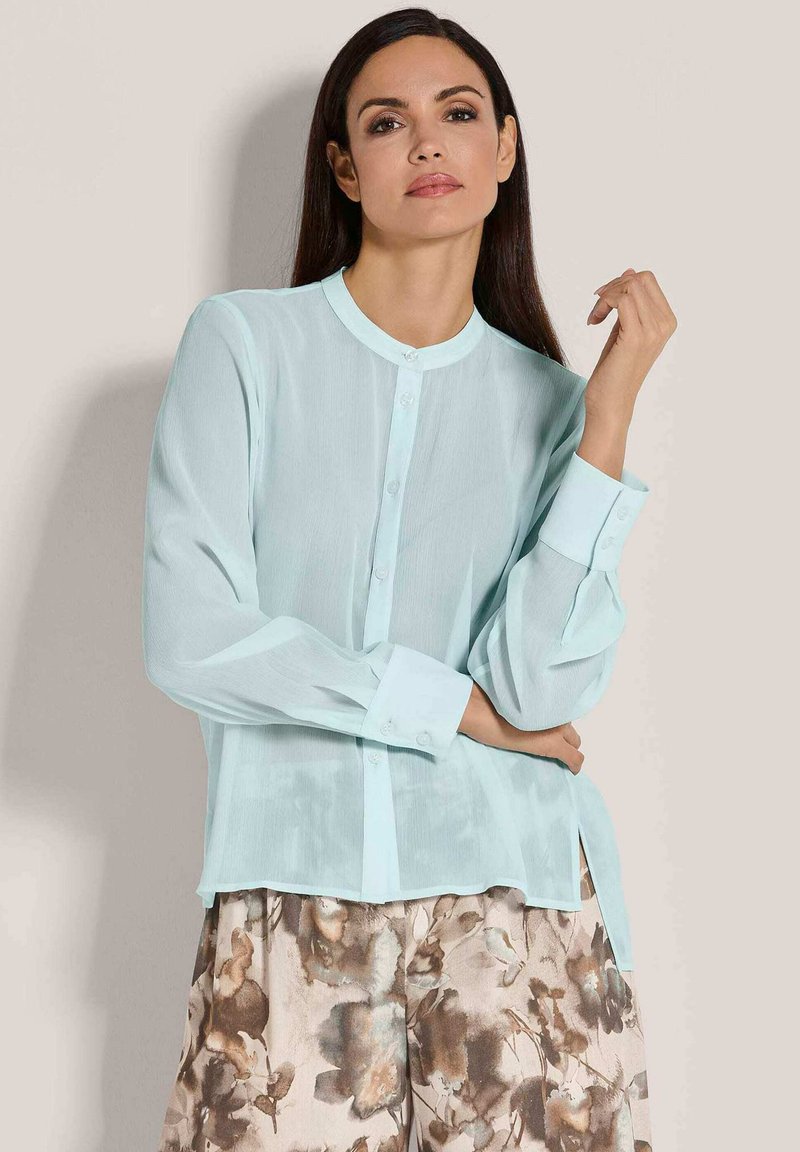 Helles blaues, durchsichtiges Blusenshirt mit rundem Halsausschnitt, Knopfleiste vorne und langen Ärmeln, kombiniert mit einer Hose im Blumendesign.