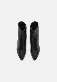 Bottes cheville en cuir noir avec des bouts pointus et des fermetures éclair latérales, vues de dessus sur un fond clair.