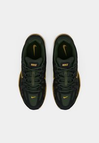 Pantofi sport Nike cu o parte superioară din plasă verde închis, detalii negre, accente aurii și o talpă din cauciuc texturat. Dispun de șireturi și logo.