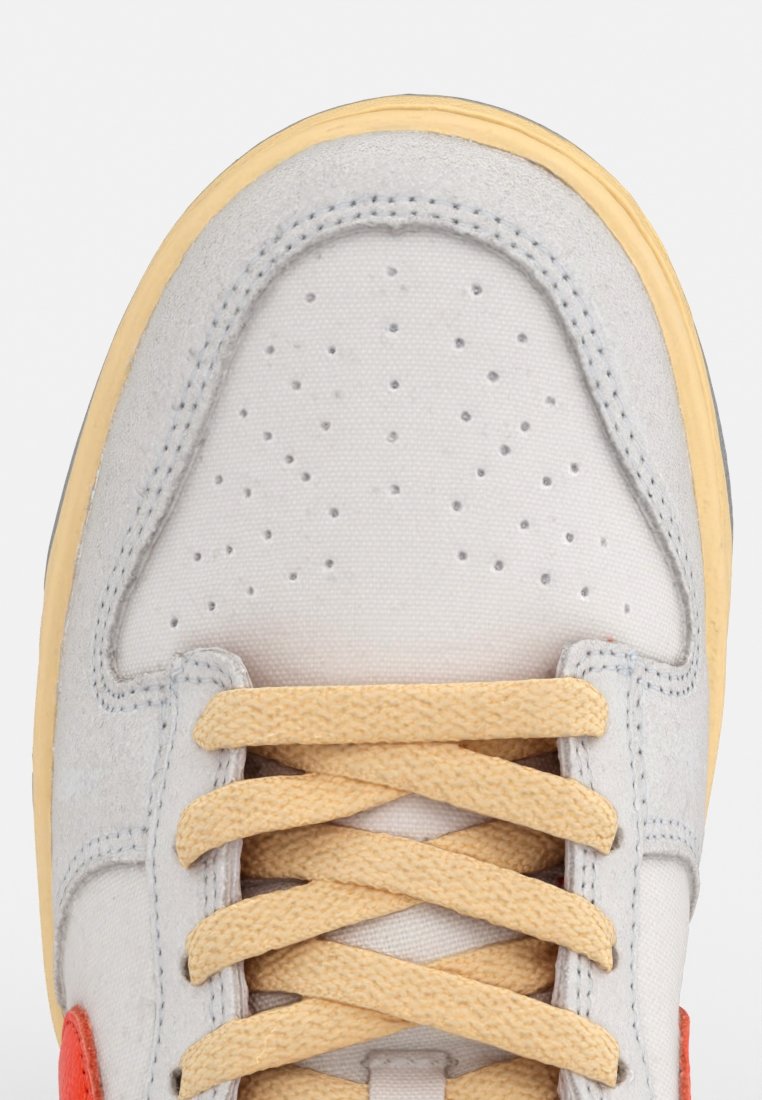 Tomaia in suede grigio con perforazioni, suola in gomma gialla e lacci beige. Presenta dettagli rossi ai lati e una finitura testurizzata.