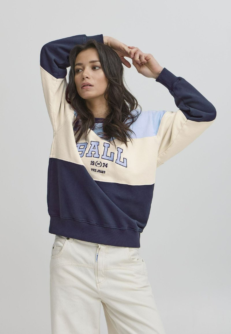 Fargeblokkgenser i beige, navy og lyseblå. Har grafikk med "BALL 1974". Mykt materiale med ribbede mansjetter og kant. Ledig passform.