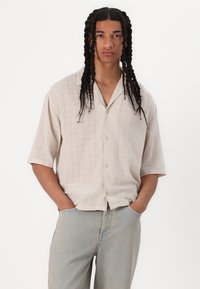 Hellbeige Kurzarmhemd mit Karomuster, mit Kragen und Knopfverschluss, kombiniert mit hellblauen Jeans.