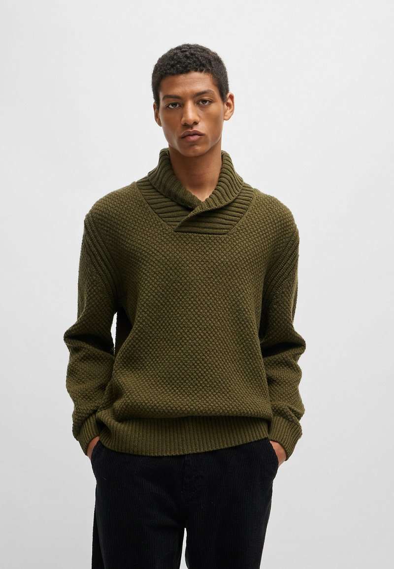Suéter de punto en verde oliva oscuro con un patrón texturizado, amplio cuello doblado y corte relajado. Combina con pantalones de pana negros.