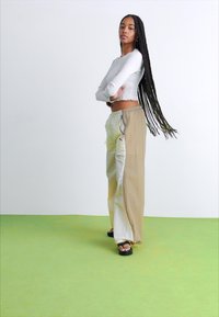 Pantalones cargo largos y ligeros en beige y blanco, con bolsillos laterales y cintura con cordón, combinados con una blusa ajustada blanca y sandalias negras.