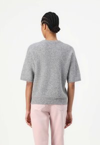 Gray short-sleeve sweater made of soft textured fabric, with a round neckline and a relaxed fit, paired with light pink jeans.