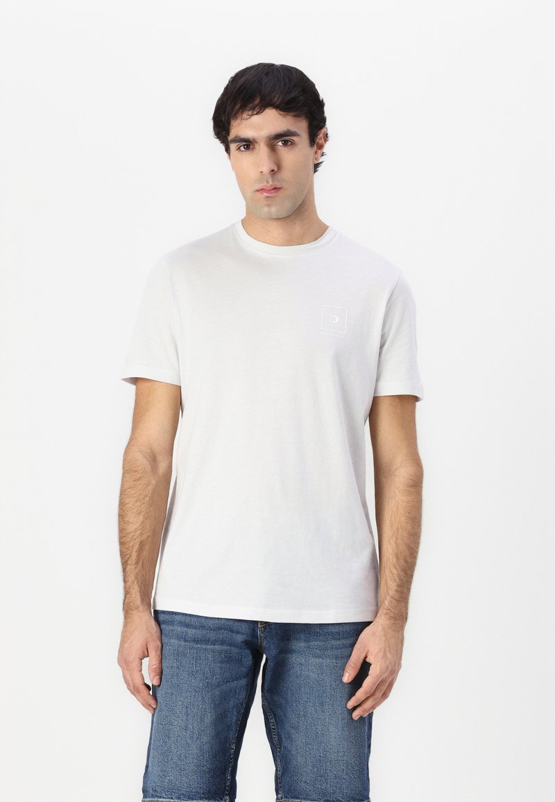 Hvit bomulls t-skjorte med rund hals og korte ermer, prydet med en liten firkantet logo på venstre bryst, iført med denimshorts.
