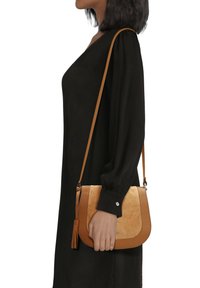 Tan schoudertas met een suède voorkant en gladde leren accenten. Bevat een kwastdetail en een lange verstelbare strap.