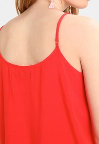 Haut rouge sans manches avec fines bretelles, présentant une texture lisse et un design au dos. Aucun motif ou ornement visible.