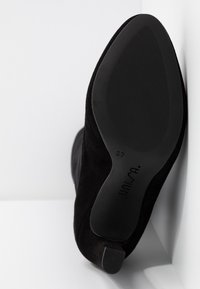 Chaussure en daim noir avec une semelle texturée, présentant une forme élégante et courbée ainsi qu'un petit talon. Marquée "37" et "UNISA" en dessous.