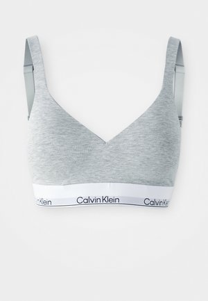 Brassière gris clair en tissu doux, avec un design triangulaire et des bretelles réglables, ornée d'une bande blanche affichant le texte "Calvin Klein".