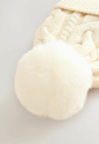 Balta adīta cepure ar lielu, mīkstu mākslīgā kažoka pom-pom. Audums ir biezs un vītņu adījums ar ribotu joslu.