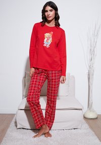 Punane pikkade varrukatega pidžaamatopp, millel on karu kujutis; punased ja valged ruudulised püksid, lõdva lõikega. Pehme kangas, mugav disain.