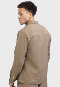Brown textured shirt with a collared neckline and button cuffs, featuring a relaxed fit and visible stitching detail on the back.