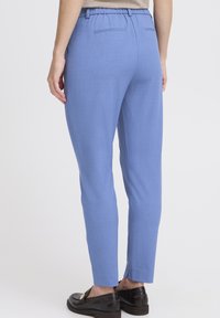 Pantaloni azzurri chiari con vita elastica, design a gamba affusolata e due tasche posteriori. Il materiale appare liscio con una sottile texture.