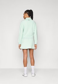 Mintgrön sweatshirt med krage och ribbade muddar, tillsammans med en matchande kjol. Har en logotyp på baksidan. Slät textur.