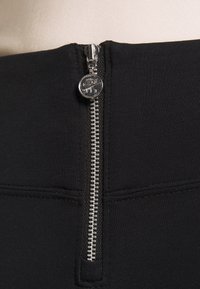 Närbild av en svart klädesdragkedja med en silverdragningsflik som har Nike Air-logotypen på ribbat tyg.