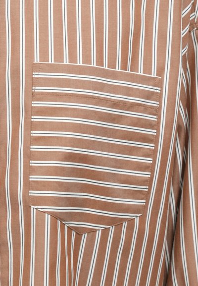 Barna ing fehér függőleges csíkokkal. Mellkasán zsebével, mely hegyes zsebfedővel rendelkezik. Simább textúra, laza kialakítás, és könnyű anyag.