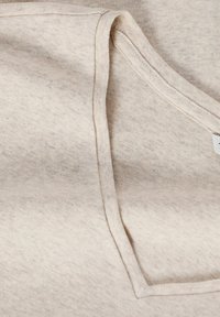Gros plan d'un tissu beige avec des coutures formant un col en V sur un vêtement en coton doux.