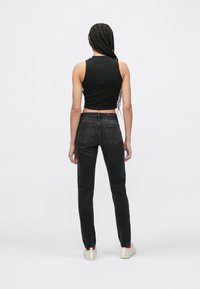 Čierny skrátený tielko a čierne rifle s rovnými nohavicami. Hladká tkanina, priliehavý strih a zadné vrecká na rifliach. Obuv je biela s červenými detailmi.