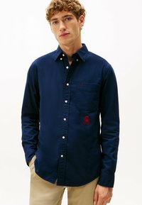 Marineblauwe button-up shirt van katoen, met een borstzak en een rood geborduurd logo. Soepele textuur en lange mouwen.