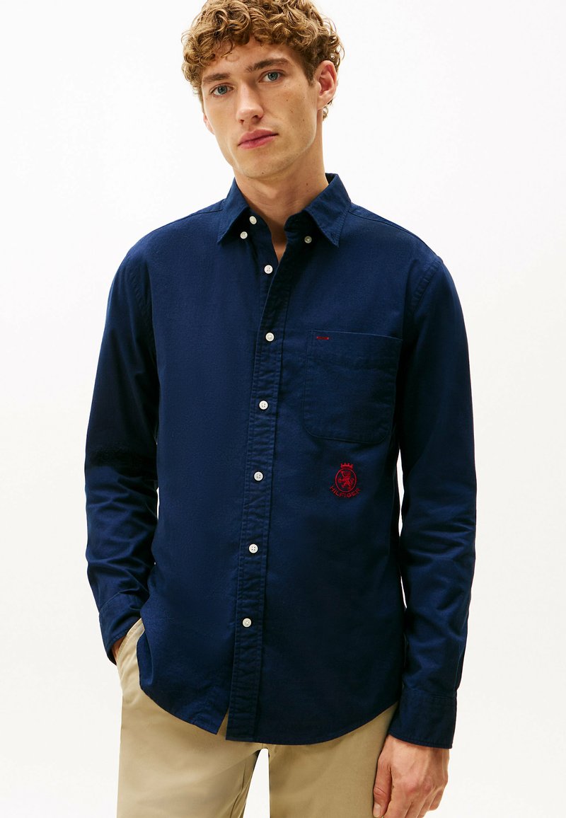 Marineblauwe button-up shirt van katoen, met een borstzak en een rood geborduurd logo. Soepele textuur en lange mouwen.