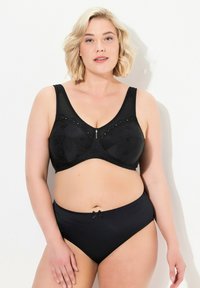 Sosten negro con estampado floral, tirantes anchos y detalles decorativos. Braguitas negras de tiro alto con un pequeño lazo en el centro.