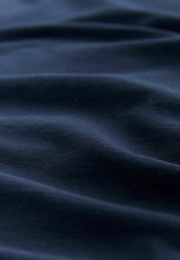 Mīksts tumši zils audums ar maigām krokām un gludu tekstūru, radot vieglas ēnas un izgaismojumu.