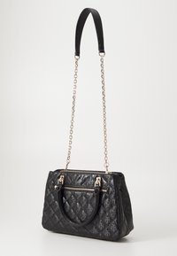 Sac à main matelassé noir avec une bandoulière chaîne dorée, deux poignées courtes et une poche zippée à l'avant, sur un fond uni clair.