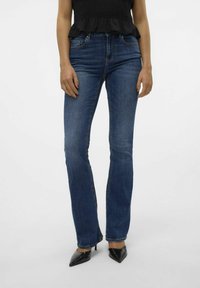 Blå denimjeans med slim fit, lätt utsvängda, femfickorsdesign och kontrasterande sömmar, tillsammans med svarta spetsiga klackar.